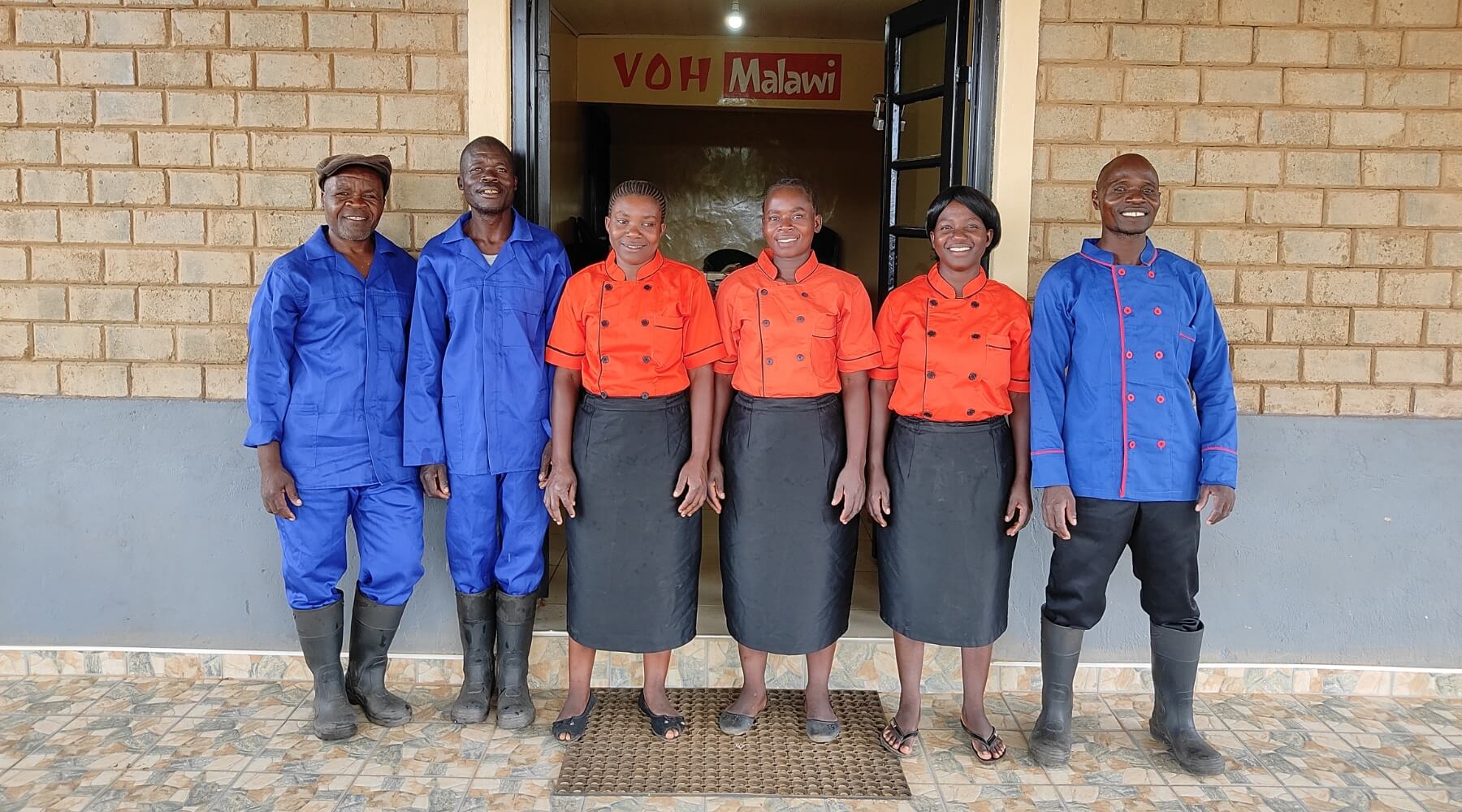 Five staff members standing in the entrance of VOH Malawi, wearing new uniforms and smiling. 