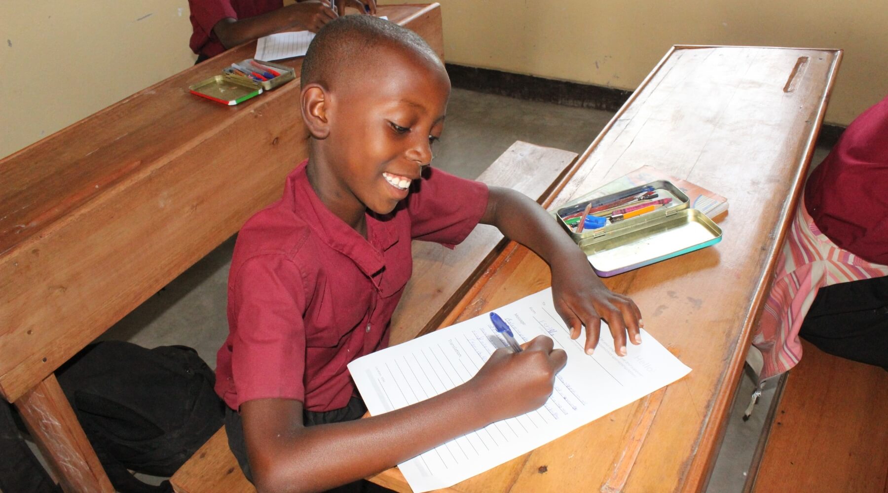 A child sitting at a desk, writing a letter and smiling.