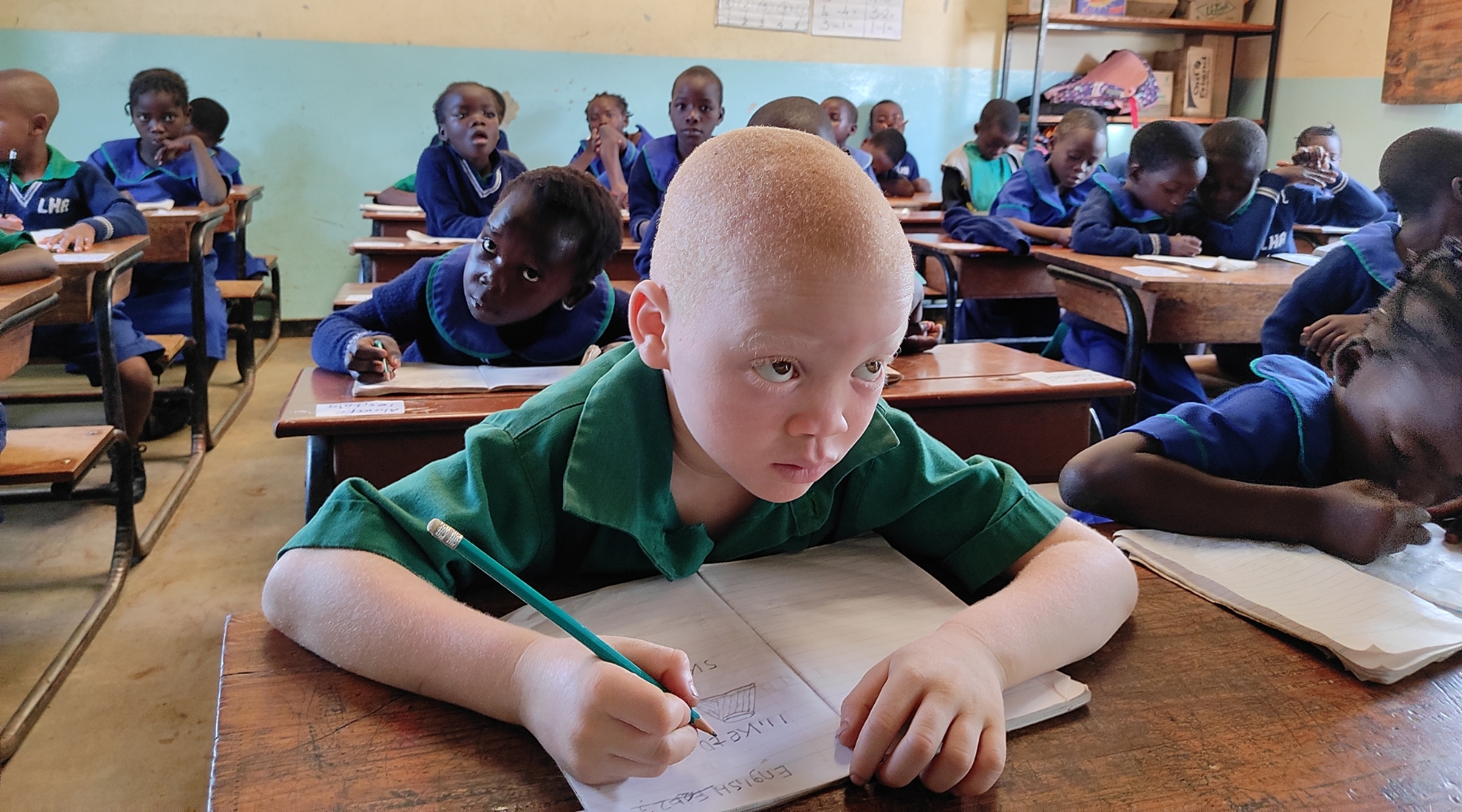 A young boy sitting at his desk in a classroom full of students. 
