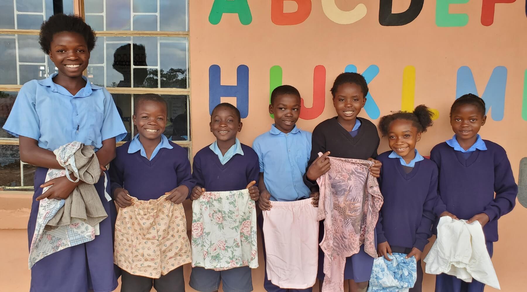 A group of children standing outside holding new clothes, smiling at the camera. 
