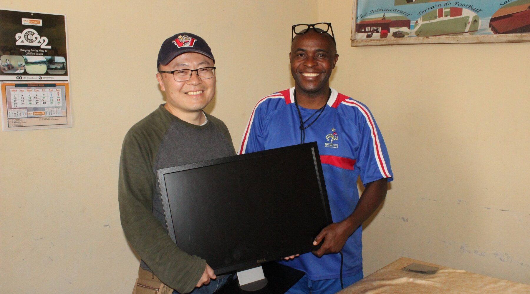 A man holding a desktop computer and handing it to another man, smiling.
