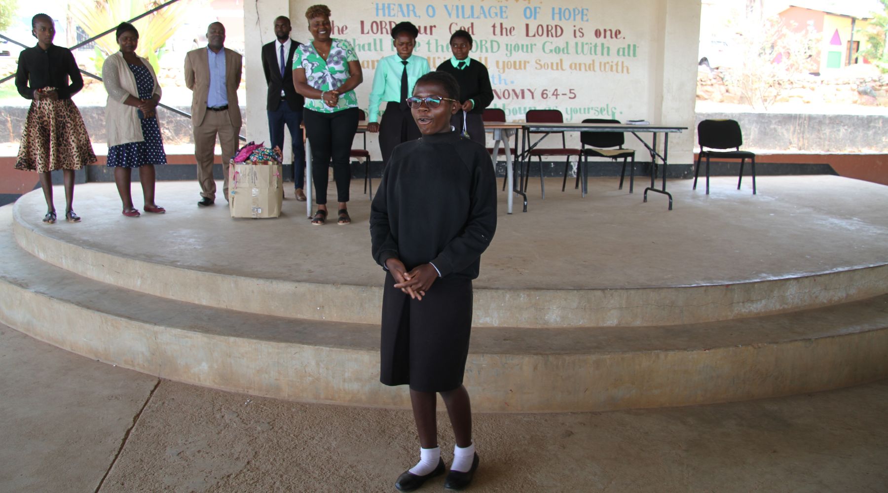 2024.10.28-chongwe A young person speaking on a stage with a group of adults behind