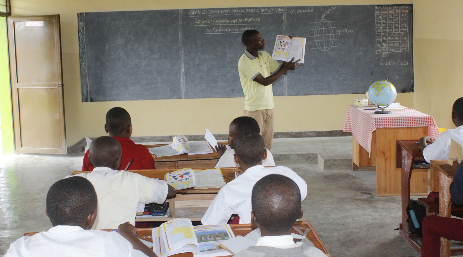 2024.10.28-maramvya A teacher holding a textbook at the front of a classroom full of students