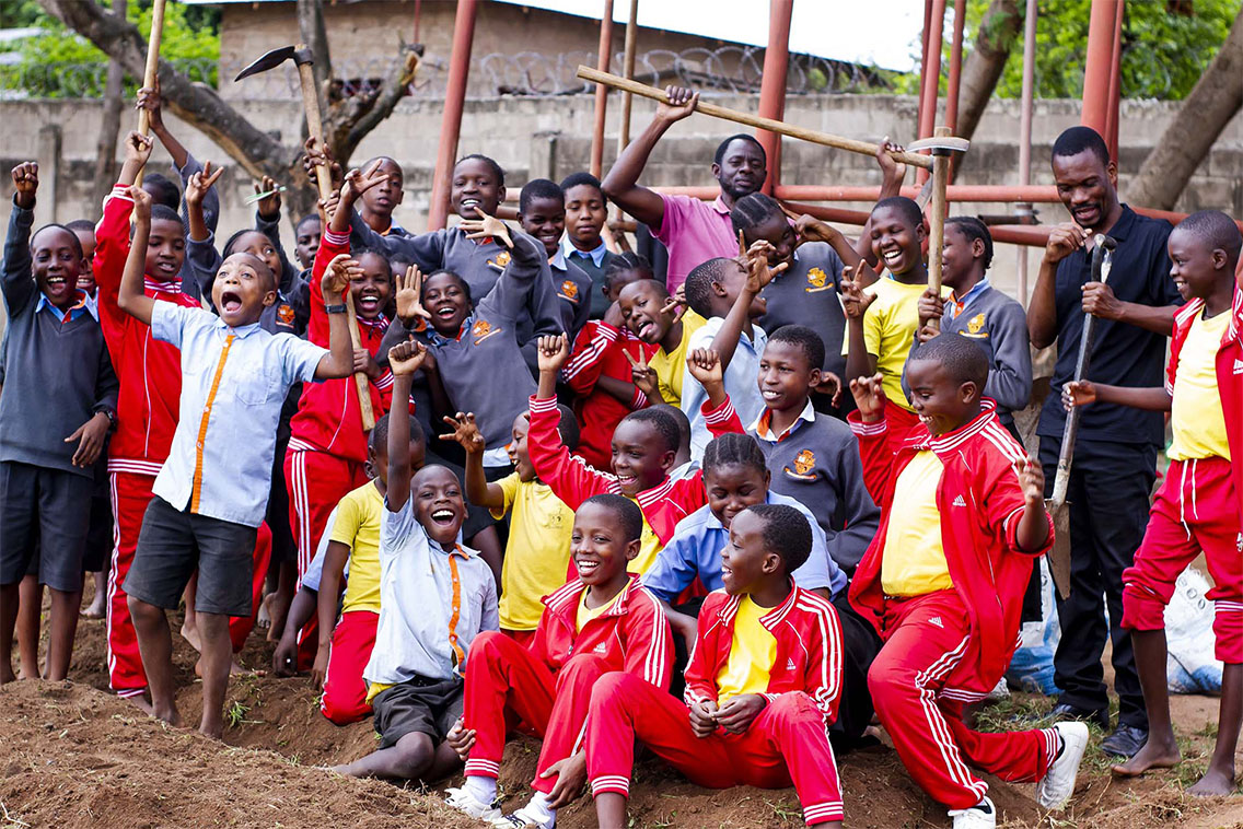 A large group of young people holding garden equipment and waving at the camera.