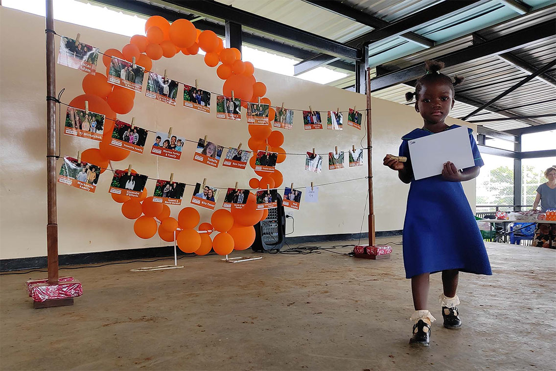 Young girl holding a picture with a display of photos and balloons behind her.