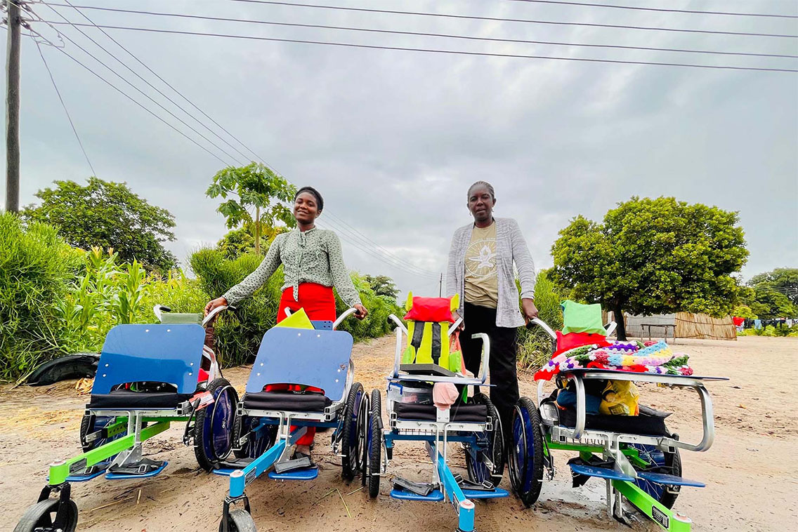 Two adults standing with four wheelchairs.
