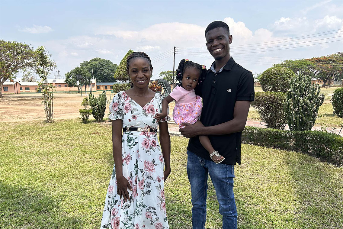 A young woman standing with a young man who is holding a small toddler with pigtails.