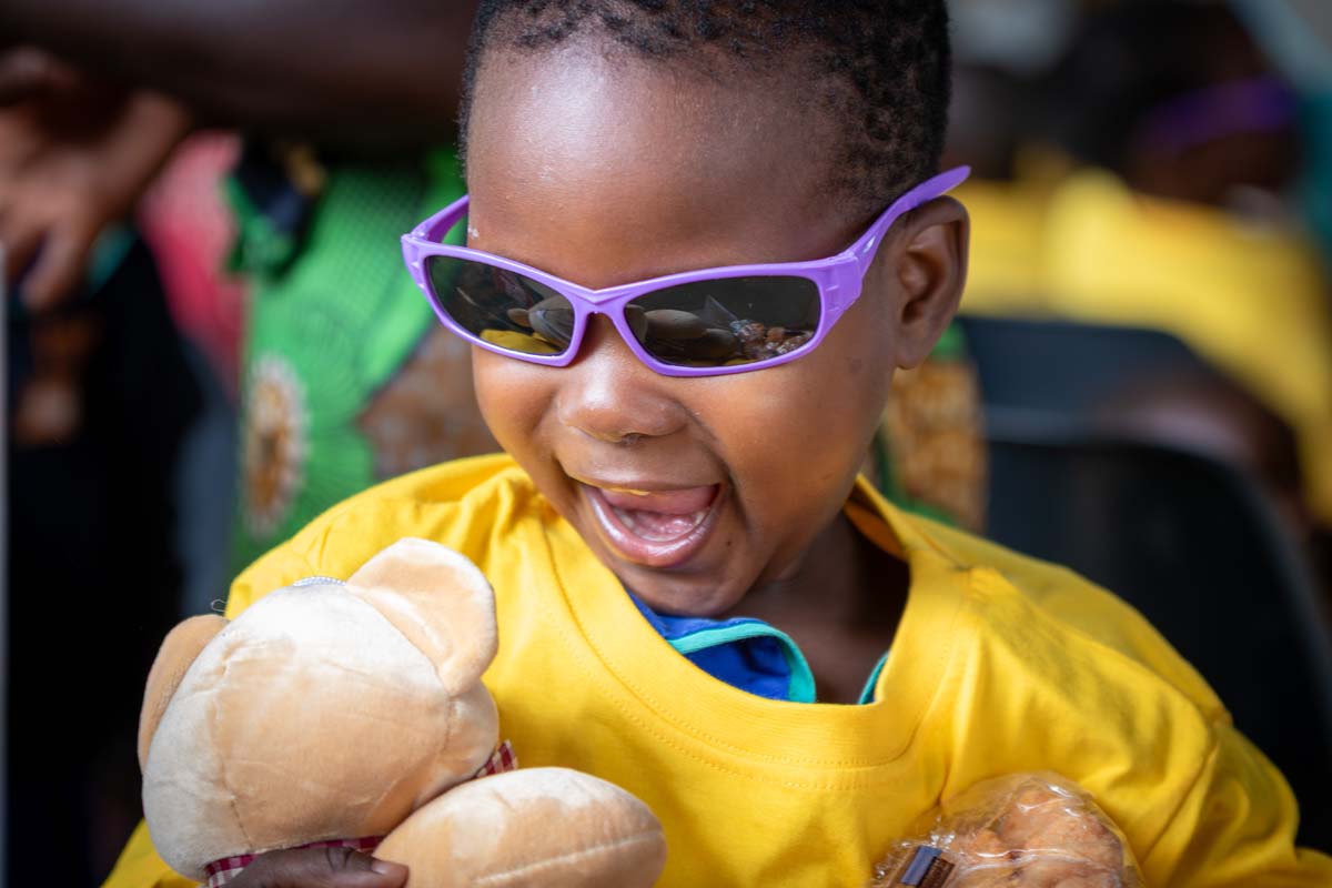 child wearing sunglasses and holding a teddy bear with a big smile